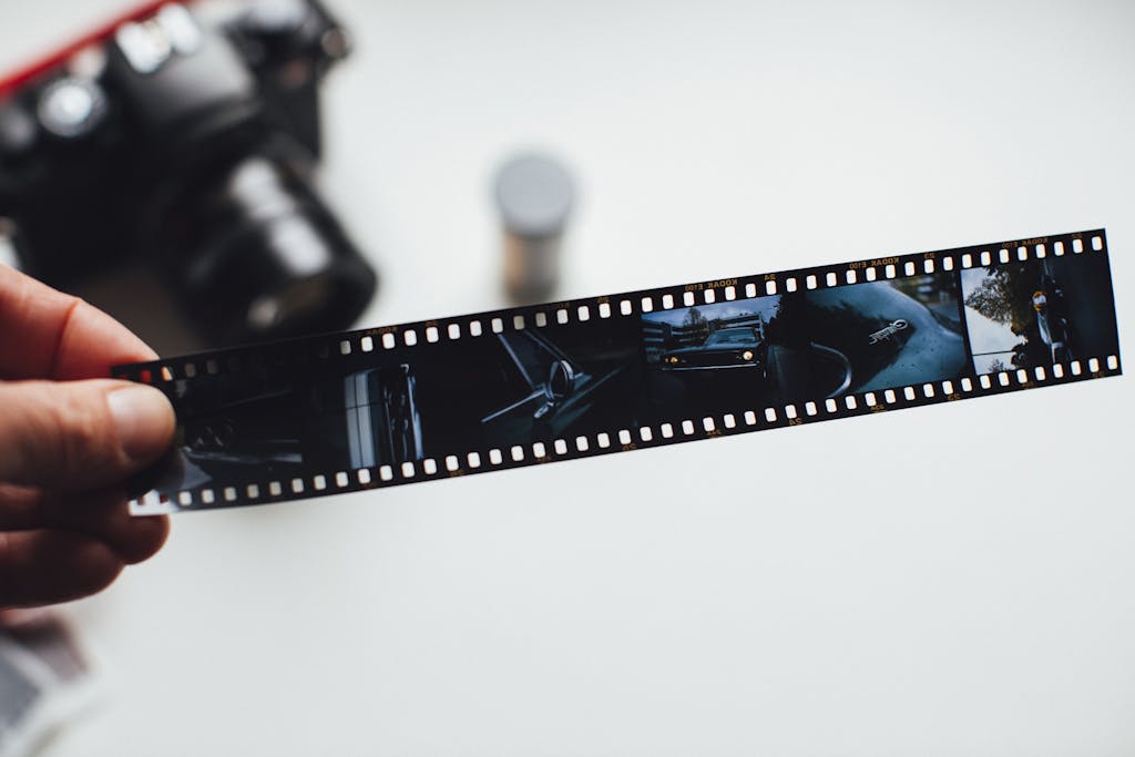 Close-up of a hand holding a vintage film strip with a blurred camera in the background, evoking nostalgia.